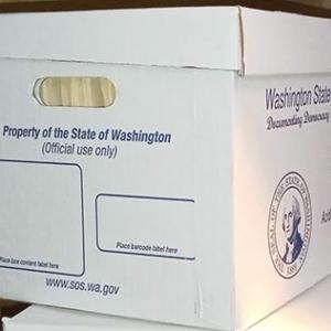 The front and side of a white box with blue lettering. The shorter front side says "Property of the State of Washington (Official use only)." There are also outlined areas for affixing labels. The longer side has blurry printing but is branded for the Washington State Archives and includes the state seal.